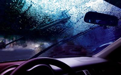 Вождение автомобиля под дождем по мокрой дороге. дождливая погода через  окно машины. дождь сквозь лобовое стекло движущейся машины. вид через окно  машины под дождем. дворники лобового стекла автомобиля включены в дождь. |